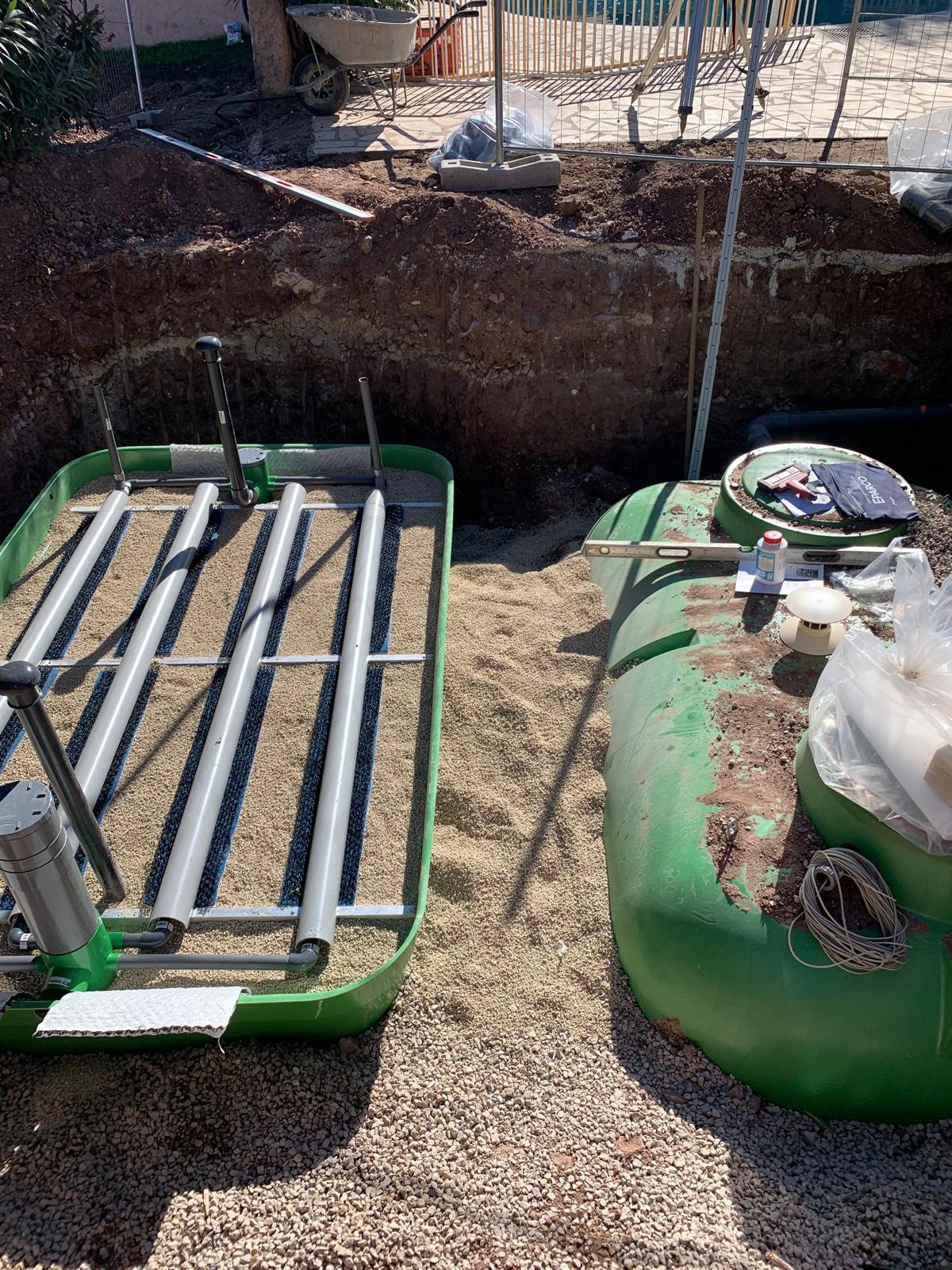 Deux cuves vertes, une fosse septique et un filtre à sable, sont installées dans une fosse de terrassement sur un lit de gravier.